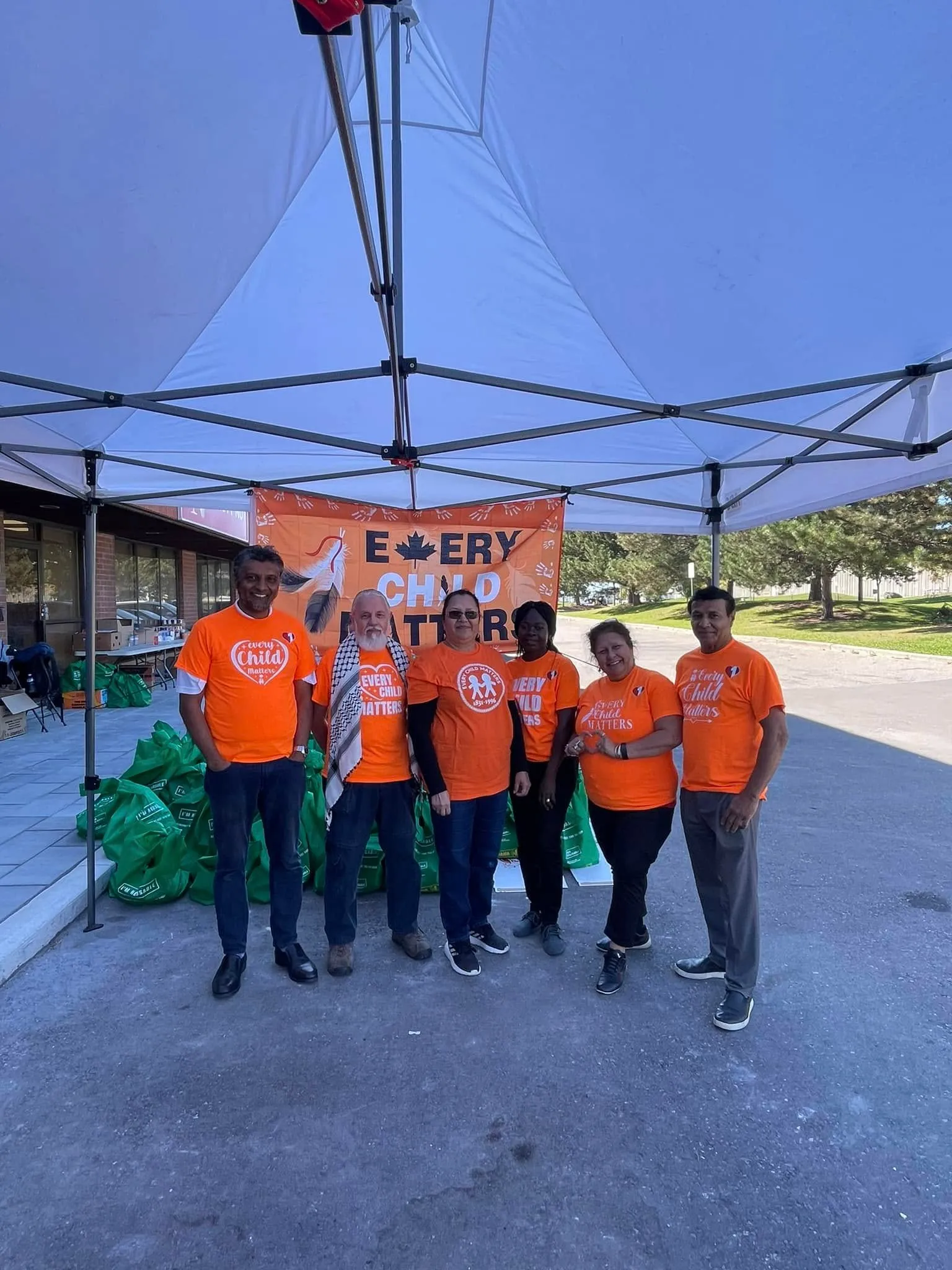 A group of One Love volunteers in orange shirts beneath an Every Child Matters banner