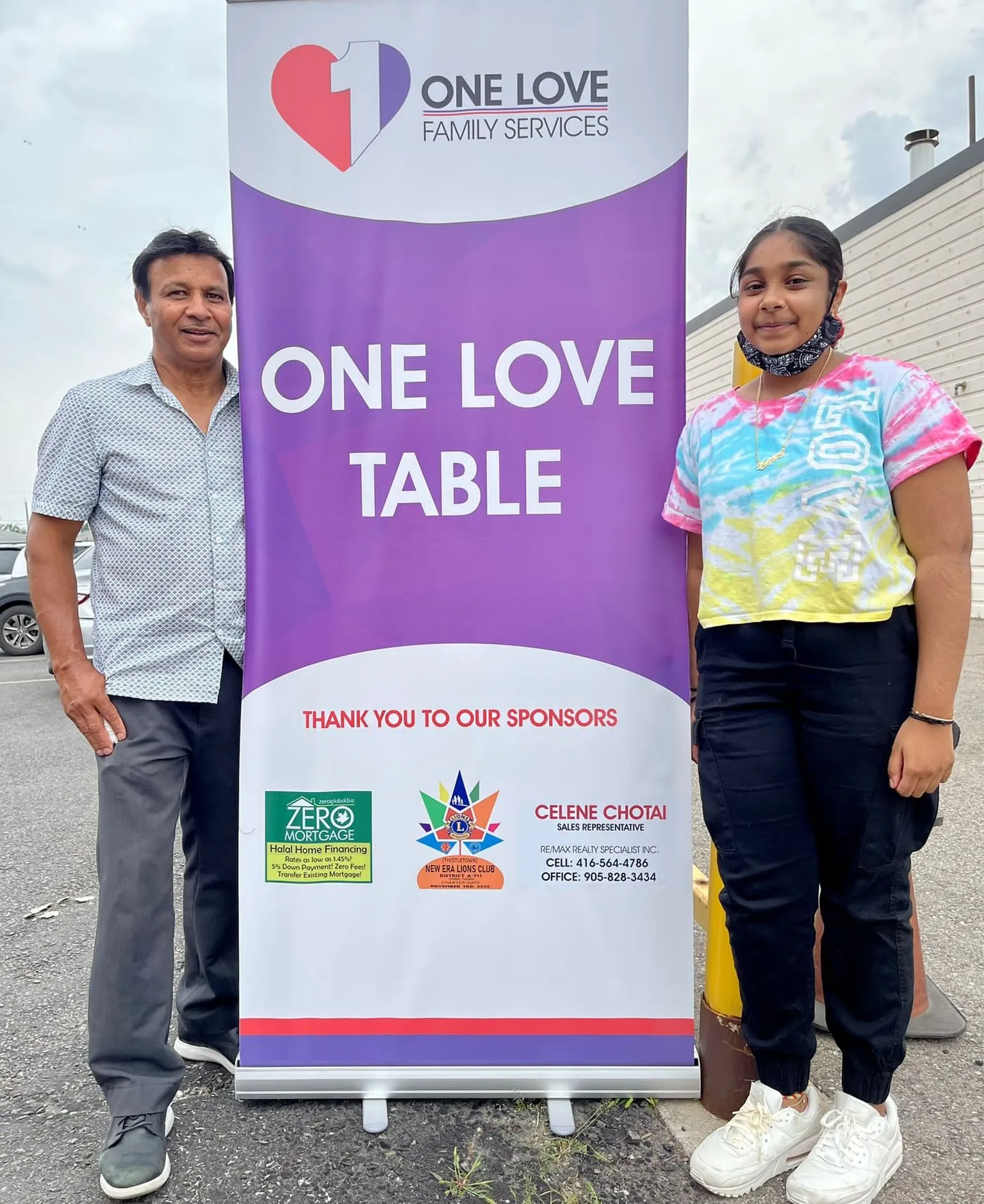 Two volunteers beside the One Love Table banner at a food distribution